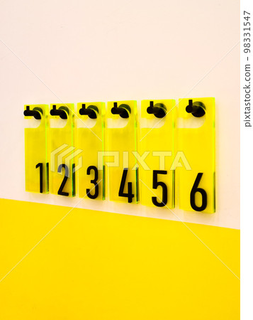 Black numbers one to six on yellow plexiglass plates hang on the wall on black hooks 98331547
