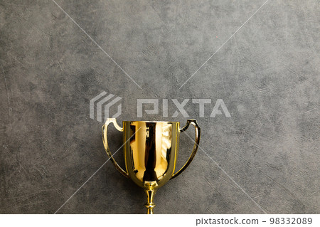 Simply flat lay design winner or champion gold trophy cup on concrete stone grey background. Victory first place of competition. Winning or success concept. Top view copy space Simply flat lay design winner or champion gold trophy cup on concrete stone grey background. Victory first place of competition. Winning or success concept. Top view copy space 98332089