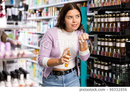 Satisfied young woman chooses and tries perfume in cosmetics store 98332856