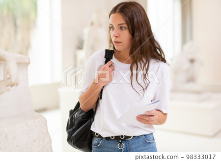 Focused girl visitor looks with interest at the sculpture in the museum hall 98333017