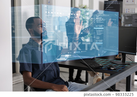 African american programmer working with hologram checking data while creating security system. Using holographic image and new interface for cloud computing, database code programming. African american programmer working with hologram checking data while creating security system. Using holographic image and new interface for cloud computing, database code programming. 98333225