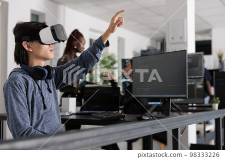 Asian software developer using virtual reality goggles to code new server interface, analyzing script information on terminal window. Coder programming it database for internet software with vr Asian software developer using virtual reality goggles to code new server interface, analyzing script information on terminal window. Coder programming it database for internet software with vr 98333226