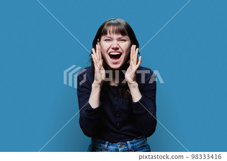 Emotional young female screaming at camera, on blue background Emotional young female screaming at camera, on blue background 98333416