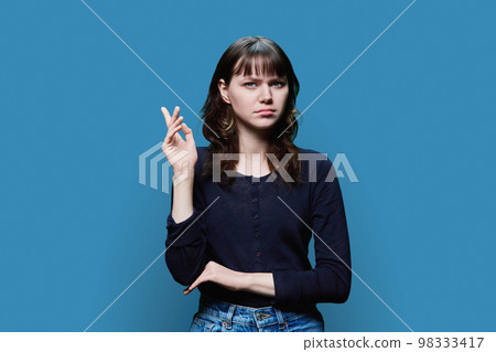 Dissatisfied young female looking at camera on blue background Dissatisfied young female looking at camera on blue background 98333417