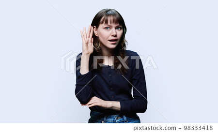 Young female holding hand near ear, listening attentively, on white background Young female holding hand near ear, listening attentively, on white background 98333418