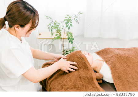 A woman who receives a head / scalp massage at a chiropractic clinic and a therapist, a chiropractor, a masseuse (manipulative clinic / salon) 98335790