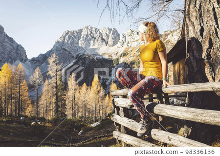 Woman hiker sitting on a wooden fence, while hiking on a beautiful autumn day 98336136