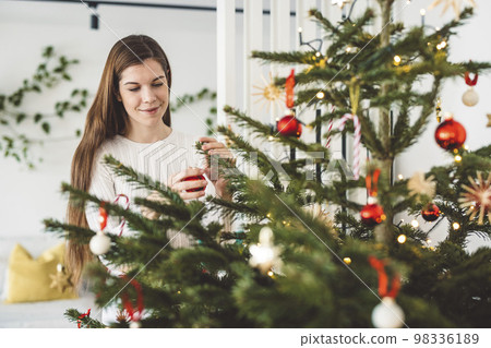 Woman decorating the Christmas tree with festive red ornaments  98336189