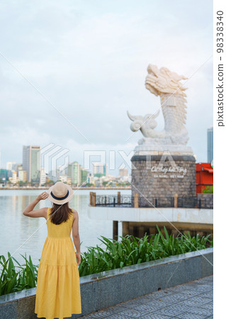 Woman Traveler with yellow dress visiting in Da Nang. Tourist sightseeing the river view with Carp Dragon Statue or Ca Chep Hoa Rong.Landmark and popular. Vietnam and Southeast Asia travel concept Woman Traveler with yellow dress visiting in Da Nang. Tourist sightseeing the river view with Carp Dragon Statue or Ca Chep Hoa Rong.Landmark and popular. Vietnam and Southeast Asia travel concept 98338340