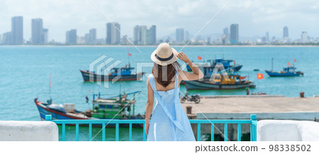 Woman traveler visiting at Son Tra marina. Tourist with blue dress and hat traveling in Da Nang city. Vietnam and Southeast Asia travel concept Woman traveler visiting at Son Tra marina. Tourist with blue dress and hat traveling in Da Nang city. Vietnam and Southeast Asia travel concept 98338502