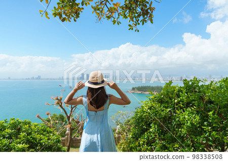 Woman traveler sightseeing Da Nang city view. Tourist with blue dress and hat traveling at Son Tra peninsula. Vietnam and Southeast Asia travel concept Woman traveler sightseeing Da Nang city view. Tourist with blue dress and hat traveling at Son Tra peninsula. Vietnam and Southeast Asia travel concept 98338508