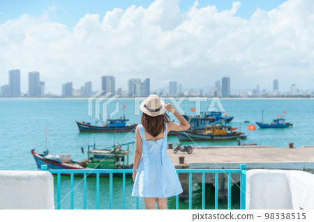 Woman traveler visiting at Son Tra marina. Tourist with blue dress and hat traveling in Da Nang city. Vietnam and Southeast Asia travel concept Woman traveler visiting at Son Tra marina. Tourist with blue dress and hat traveling in Da Nang city. Vietnam and Southeast Asia travel concept 98338515