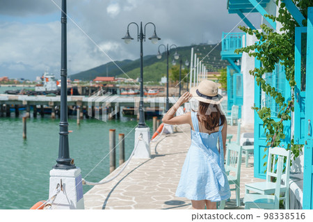 Woman traveler visiting at Son Tra marina. Tourist with blue dress and hat traveling in Da Nang city. Vietnam and Southeast Asia travel concept Woman traveler visiting at Son Tra marina. Tourist with blue dress and hat traveling in Da Nang city. Vietnam and Southeast Asia travel concept 98338516