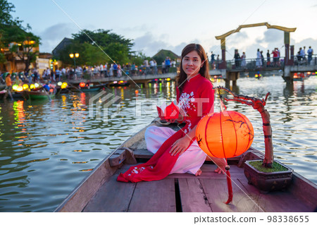 woman wearing Ao Dai Vietnamese dress, traveler Sightseeing Boat Ride and floating paper lantern at Hoi An ancient town. landmark for tourist attractions.Vietnam and Southeast travel concept 98338655