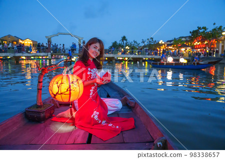 woman wearing Ao Dai Vietnamese dress, traveler Sightseeing Boat Ride and floating paper lantern at Hoi An ancient town. landmark for tourist attractions.Vietnam and Southeast travel concept 98338657