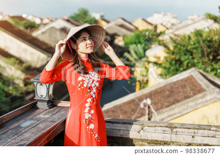 happy woman wearing Ao Dai Vietnamese dress, traveler sightseeing view at rooftop at Hoi An ancient town in Vietnam. landmark and popular for tourist attractions. Vietnam and Southeast travel concept 98338677