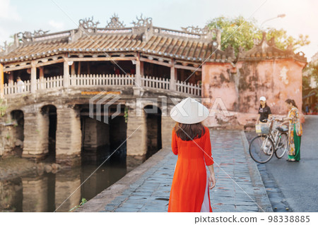 Woman traveler wearing Ao Dai Vietnamese dress sightseeing at Japanese covered bridge in Hoi An town, Vietnam. landmark and popular for tourist attractions. Vietnam and Southeast Asia travel concept 98338885