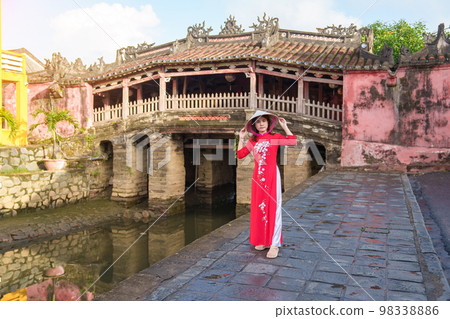 Woman traveler wearing Ao Dai Vietnamese dress sightseeing at Japanese covered bridge in Hoi An town, Vietnam. landmark and popular for tourist attractions. Vietnam and Southeast Asia travel concept Woman traveler wearing Ao Dai Vietnamese dress sightseeing at Japanese covered bridge in Hoi An town, Vietnam. landmark and popular for tourist attractions. Vietnam and Southeast Asia travel concept 98338886