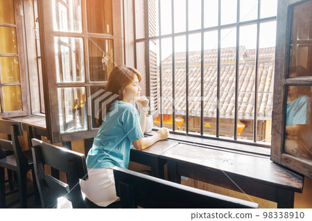 Happy woman sitting near window in the morning sunlight Happy woman sitting near window in the morning sunlight 98338910