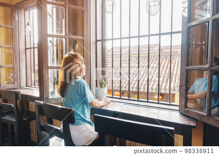 Happy woman sitting near window in the morning sunlight Happy woman sitting near window in the morning sunlight 98338911