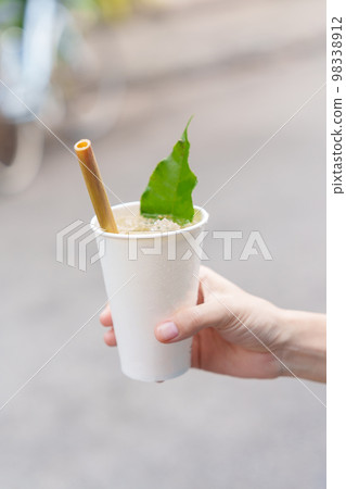 Hand holding paper cup of herbal drink with lotus petal and tea leaf, is the most popular beverage for tourists in Hoi An ancient town in central Vietnam Hand holding paper cup of herbal drink with lotus petal and tea leaf, is the most popular beverage for tourists in Hoi An ancient town in central Vietnam 98338912