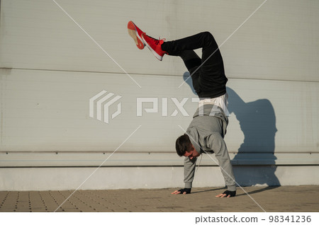 Caucasian man in hooded sweatshirt doing handstand outdoors.  98341236