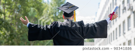 Elderly male graduate rejoices at graduation outdoors. Rear view of a man in a robe with arms outstretched to the sides.  98341886