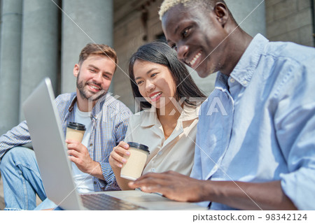 student guy and his friends using a laptop while sitting on the steps. student guy and his friends using a laptop while sitting on the steps. 98342124