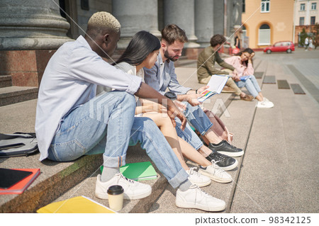students with textbooks sitting on the steps. students with textbooks sitting on the steps. 98342125