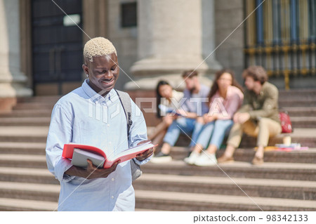 proud student with a textbook standing in front of the university. 98342133