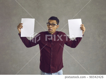 Confused black man holding two blank paper banners and trying to choose between them Confused black man holding two blank paper banners and trying to choose between them 98342426