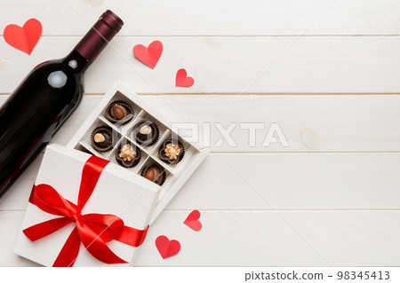 Bottle of red wine on colored background for Valentine Day with gift and chocolate. Heart shaped with gift box of chocolates top view with copy space Bottle of red wine on colored background for Valentine Day with gift and chocolate. Heart shaped with gift box of chocolates top view with copy space 98345413