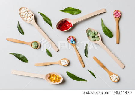 Top view Variety of vitamin and mineral pills in wooden spoon on Colored background. Top view of assorted pharmaceutical medicine pills. Dietary supplement healthcare product Top view Variety of vitamin and mineral pills in wooden spoon on Colored background. Top view of assorted pharmaceutical medicine pills. Dietary supplement healthcare product 98345479
