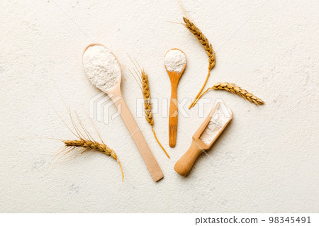 Flat lay of Wheat flour in wooden bowl with wheat spikelets on colored background. world wheat crisis Flat lay of Wheat flour in wooden bowl with wheat spikelets on colored background. world wheat crisis 98345491