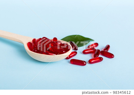 Vitamin capsules in a spoon on a colored background. Pills served as a healthy meal. Red soft gel vitamin supplement capsules on spoon Vitamin capsules in a spoon on a colored background. Pills served as a healthy meal. Red soft gel vitamin supplement capsules on spoon 98345612