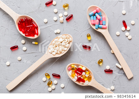 Vitamin capsules in a spoon on a colored background. Pills served as a healthy meal. Red soft gel vitamin supplement capsules on spoon 98345614
