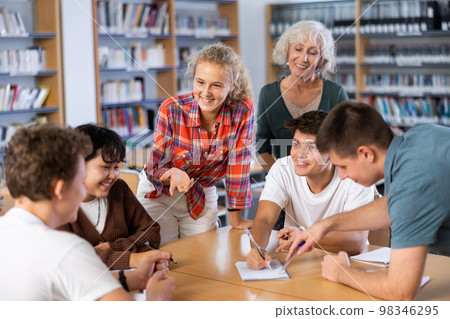 Group of schoolchildren with a female teacher in the library, discussing something 98346295