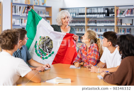Mature female teacher shows scholchildren the national flag of Mexico 98346332