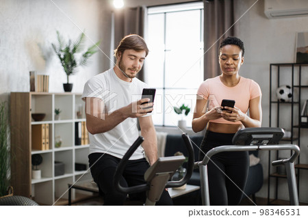 African american sports woman in sportswear running on treadmill and fit caucasian man cycling bike 98346531