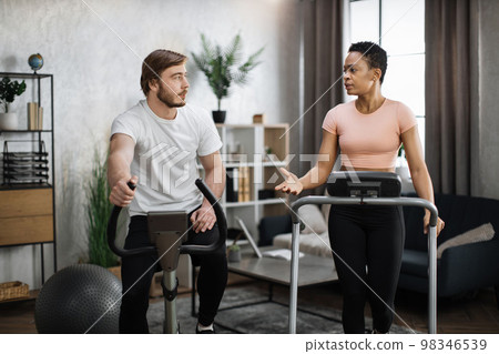 Young couple doing cardio on stationary bike and treadmill. Young couple doing cardio on stationary bike and treadmill. 98346539