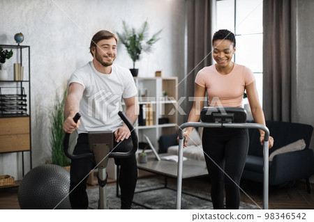 Young couple doing cardio on stationary bike and treadmill. Young couple doing cardio on stationary bike and treadmill. 98346542