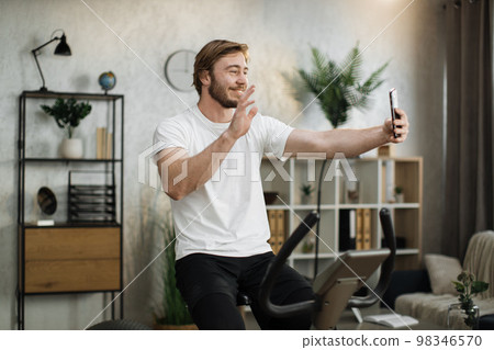 Sports bearded caucasian man in sportswear having online video call while cycling bike Sports bearded caucasian man in sportswear having online video call while cycling bike 98346570