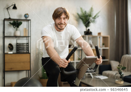 Portrait of focused young male wearing sportswear using exercise bike. 98346645