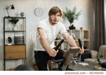 Portrait of focused young male wearing sportswear using exercise bike. 98346648