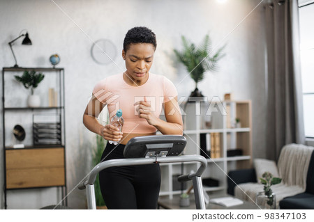 Attractive young sports african american woman holding bottle with water working out Attractive young sports african american woman holding bottle with water working out 98347103