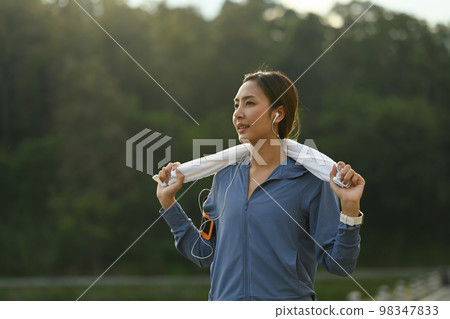 Portrait of sporty woman in sportswear and with towel resting after jogging in a green park on a sunny day Portrait of sporty woman in sportswear and with towel resting after jogging in a green park on a sunny day 98347833