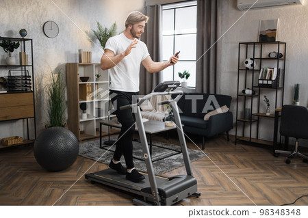 Caucasian sportsman having online video class training on smartphone using treadmill 98348348