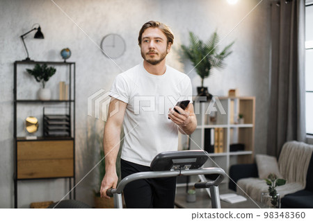 Portrait of handsome muscular man working out at home, running on treadmil Portrait of handsome muscular man working out at home, running on treadmil 98348360