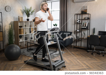 Blond bearded male in white t-shirt jogging on treadmill. Blond bearded male in white t-shirt jogging on treadmill. 98348363