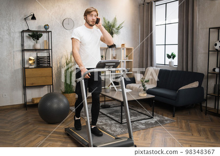 Blond bearded male in white t-shirt jogging on treadmill. Blond bearded male in white t-shirt jogging on treadmill. 98348367